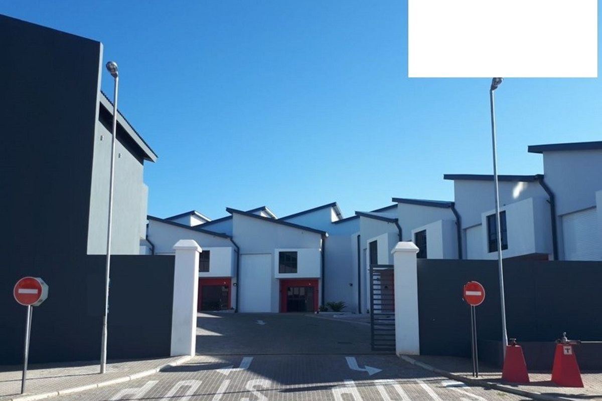 Front entrance view of a modern industrial complex featuring paved driveway access, secure perimeter walls, and multiple industrial units with roller shutter doors.