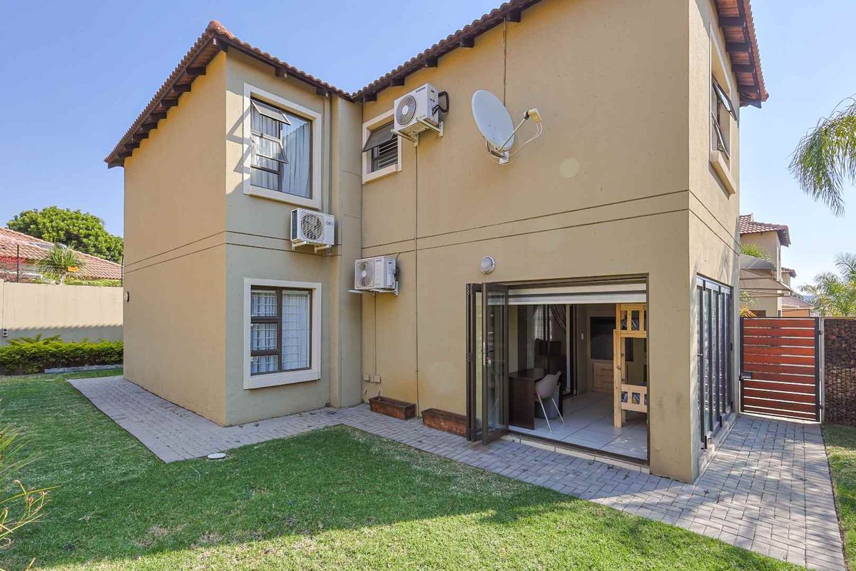 Rear view of a two-story house featuring a paved patio, bi-fold doors leading to the interior, and a well-maintained garden lawn.