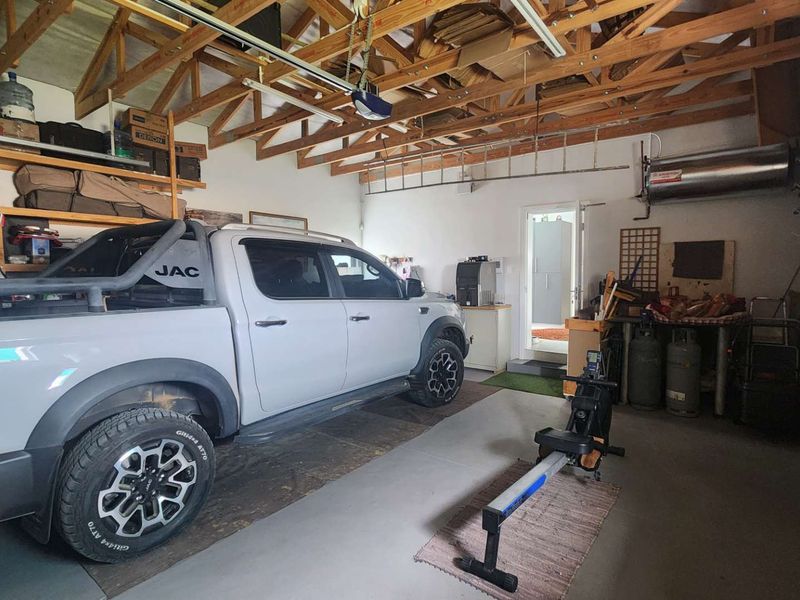 A spacious garage featuring exposed timber roof trusses, wall-mounted storage shelving, and a geyser, providing ample utility and storage space.