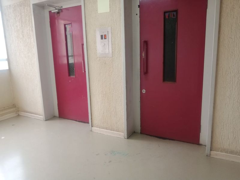 A communal hallway area featuring two red elevator doors and textured wall finishes in an apartment building.