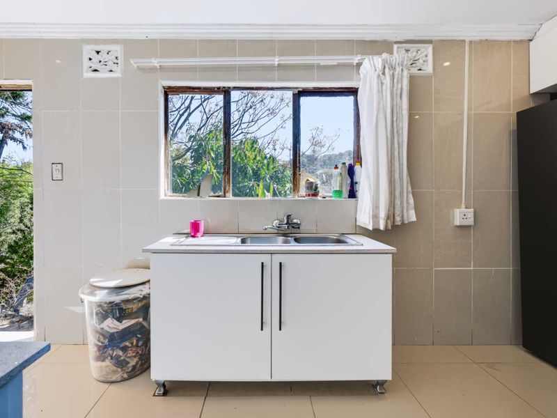 A functional laundry area featuring tiled walls, a stainless steel sink unit, and a window with natural light.