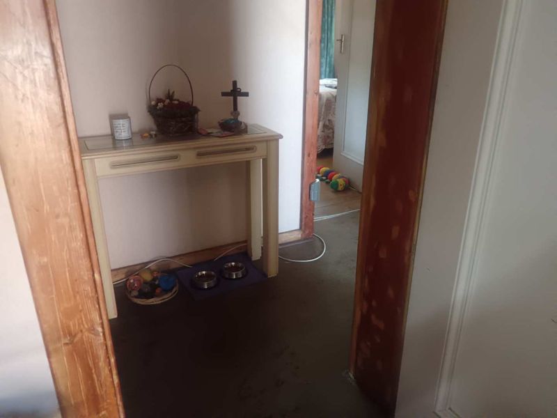 A narrow hallway featuring wooden door frames and visible wear on the flooring, leading into an adjacent room.