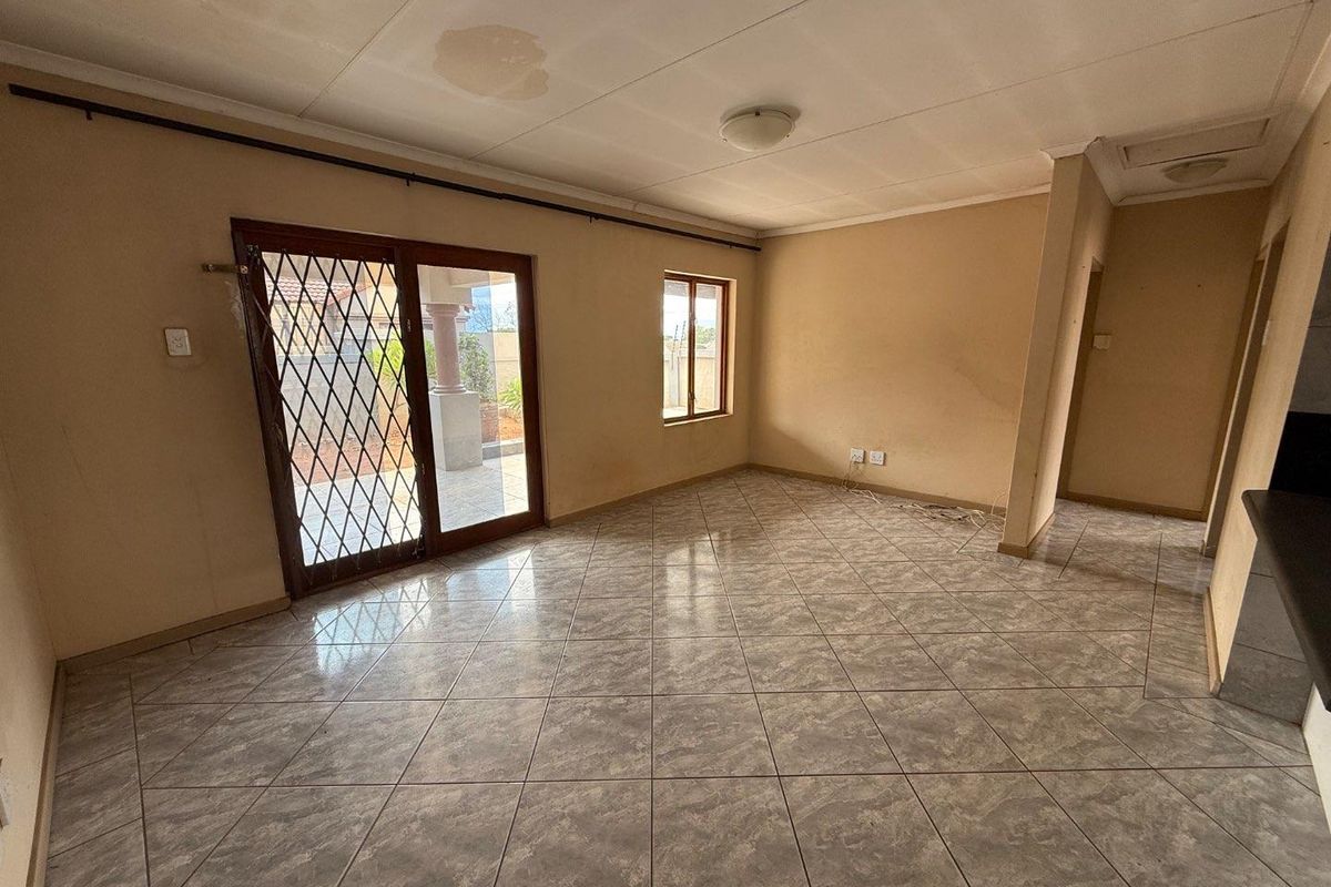 An empty living area featuring tiled flooring, a sliding glass door with security gate, and access to an outdoor patio space.