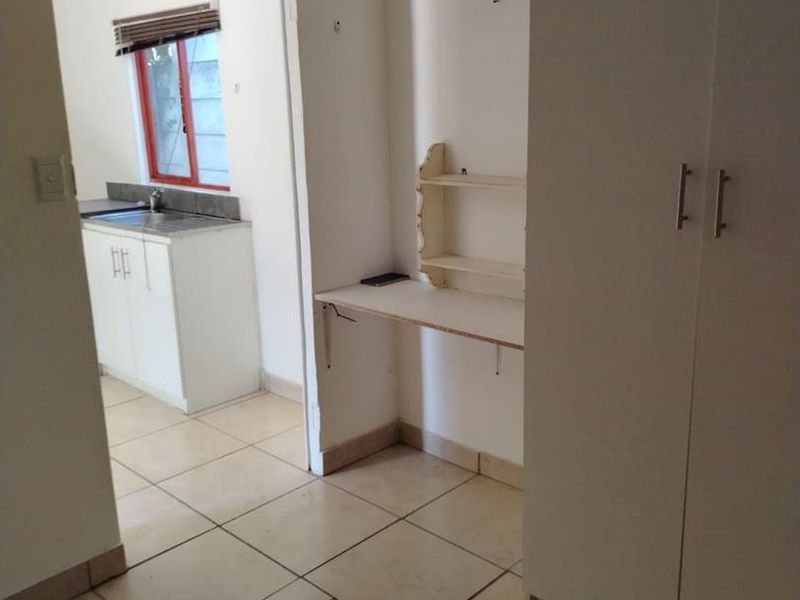 A functional hallway area featuring tiled flooring, a built-in cupboard, and a compact built-in desk with wall-mounted shelving, leading into a kitchen space.