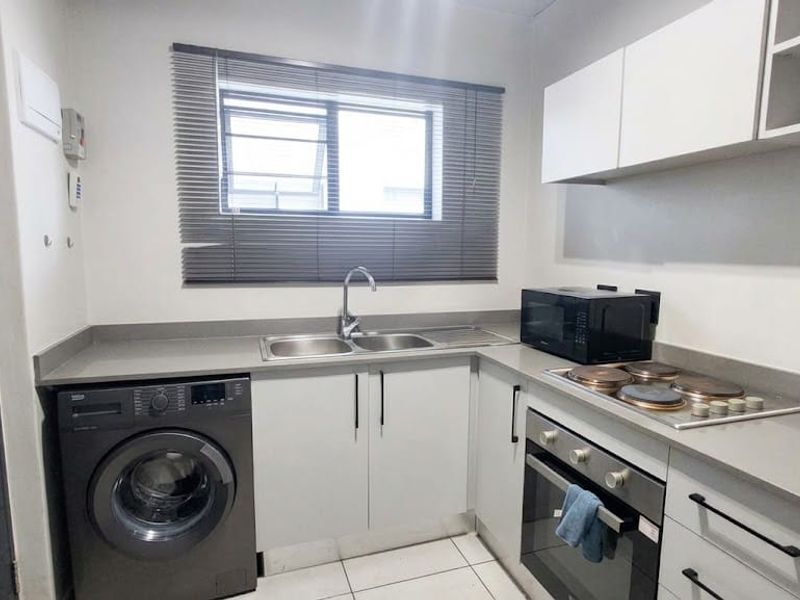 Modern kitchen featuring sleek white cabinetry, stone countertops, integrated electric hob and oven, and a stainless steel sink with a window view.