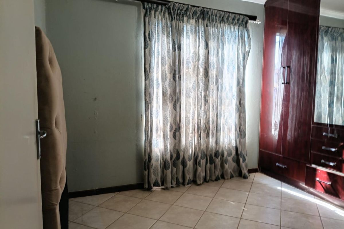 A bedroom featuring tiled flooring and a large built-in wooden wardrobe with mirrored panels.