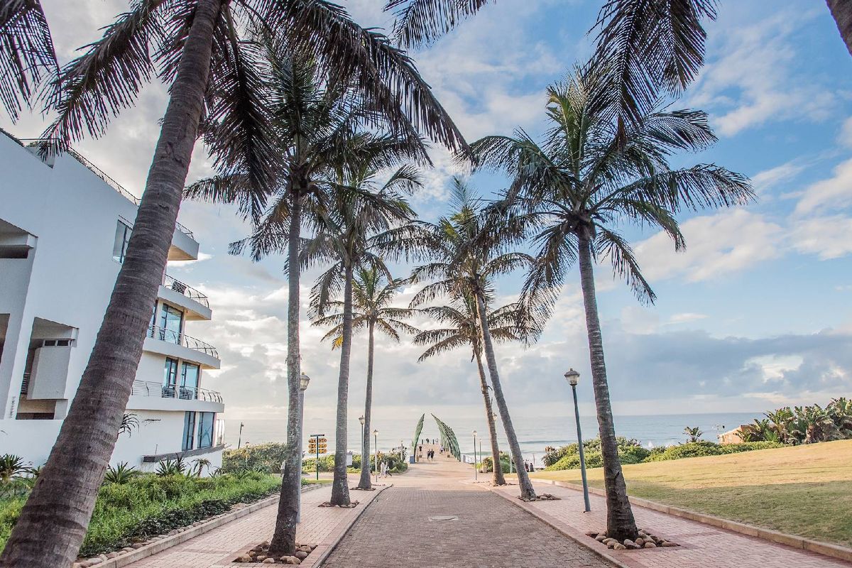 A scenic pathway lined with palm trees leading towards the ocean, adjacent to the apartment building exterior.