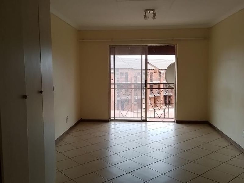 An empty bedroom featuring tiled flooring, built-in cupboards, and a sliding glass door leading to a balcony with a security gate.