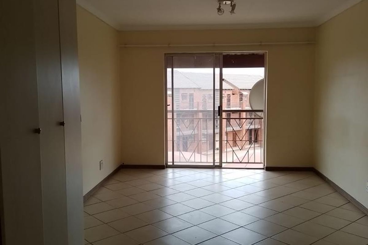 An empty bedroom featuring tiled flooring, built-in cupboards, and a sliding glass door leading to a balcony with a security gate.