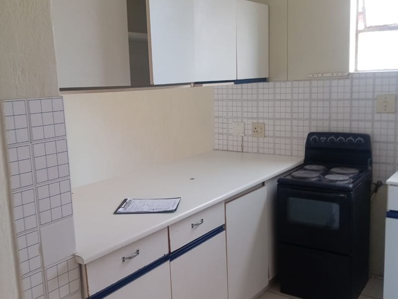 A functional kitchen featuring built-in cabinetry, laminate countertops, tiled backsplash, and a freestanding stove, ready for modernization.