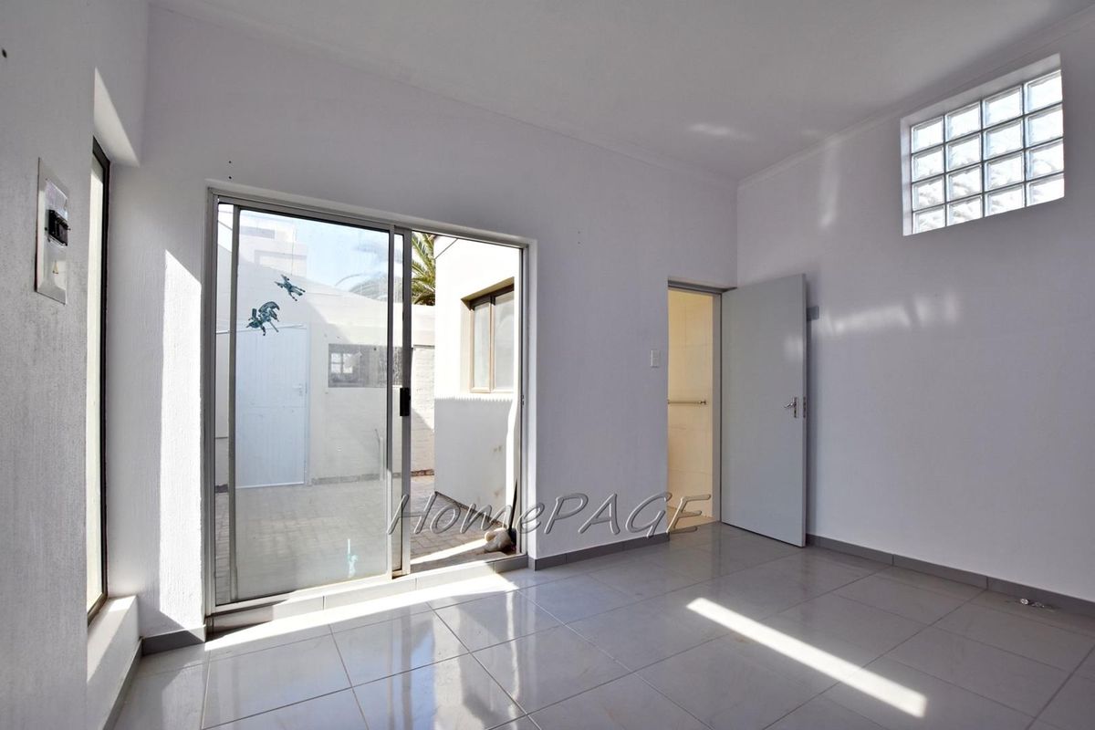 A bright, empty living area featuring tiled floors, a sliding glass door leading to an outdoor space, and a decorative glass block window.