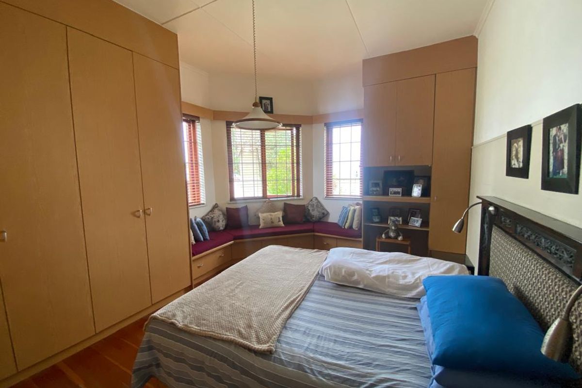 A bedroom featuring extensive built-in wooden cabinetry, a bay window with integrated seating, and polished timber flooring.