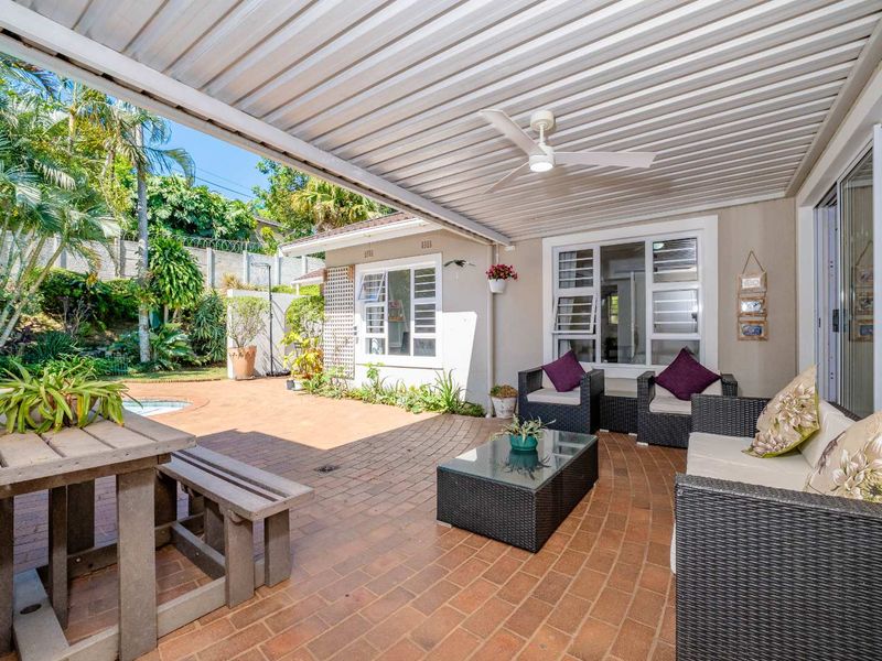 A spacious covered patio featuring brick paving, a ceiling fan, and direct access to the garden and pool area through sliding glass doors.