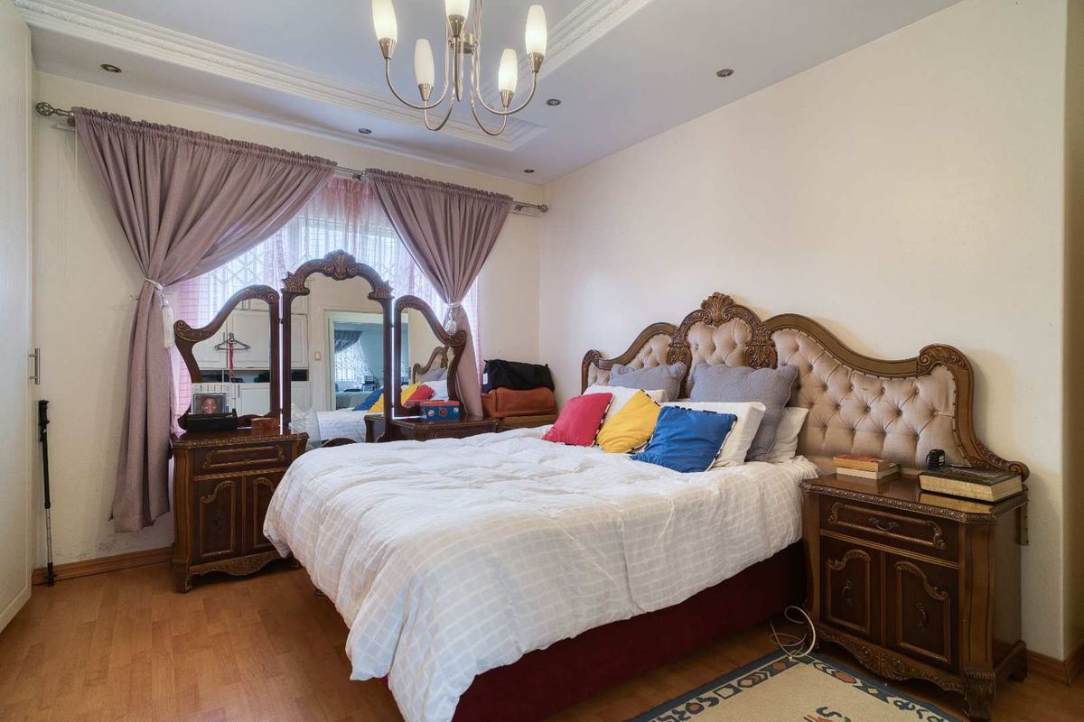 A spacious bedroom featuring laminate flooring, decorative ceiling coving, and a central chandelier, providing a comfortable and well-lit sleeping area.