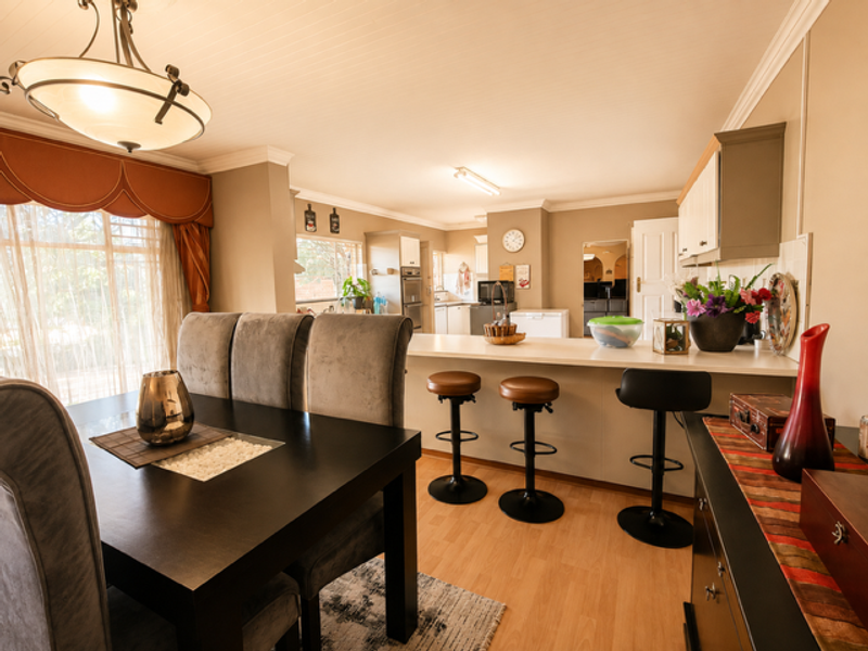 Spacious open-plan dining and kitchen area featuring a breakfast bar, built-in cabinetry, and laminate flooring, creating a functional and connected living space.