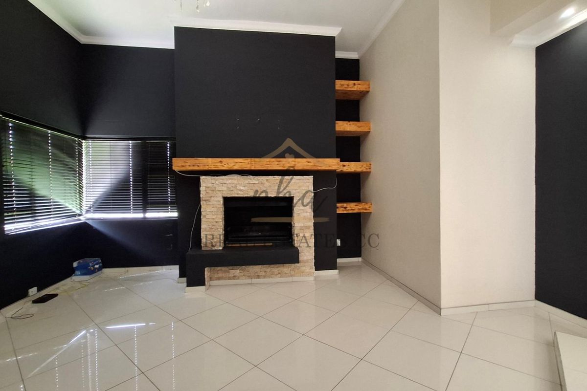 A living room featuring a stone-clad fireplace with a timber mantel and built-in wooden shelving, complemented by polished floor tiles.