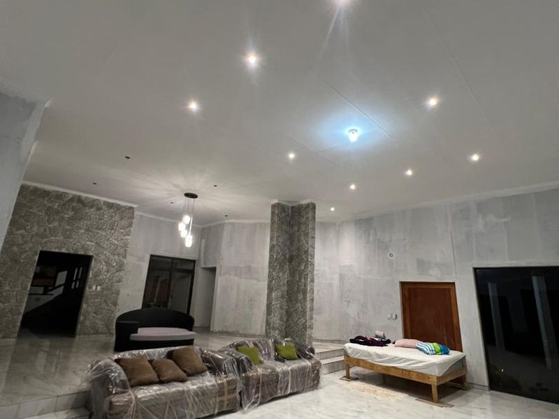 Spacious living area featuring marble-look floor tiles, stone-clad feature walls, and recessed downlights, currently undergoing final wall finishing and plastering.