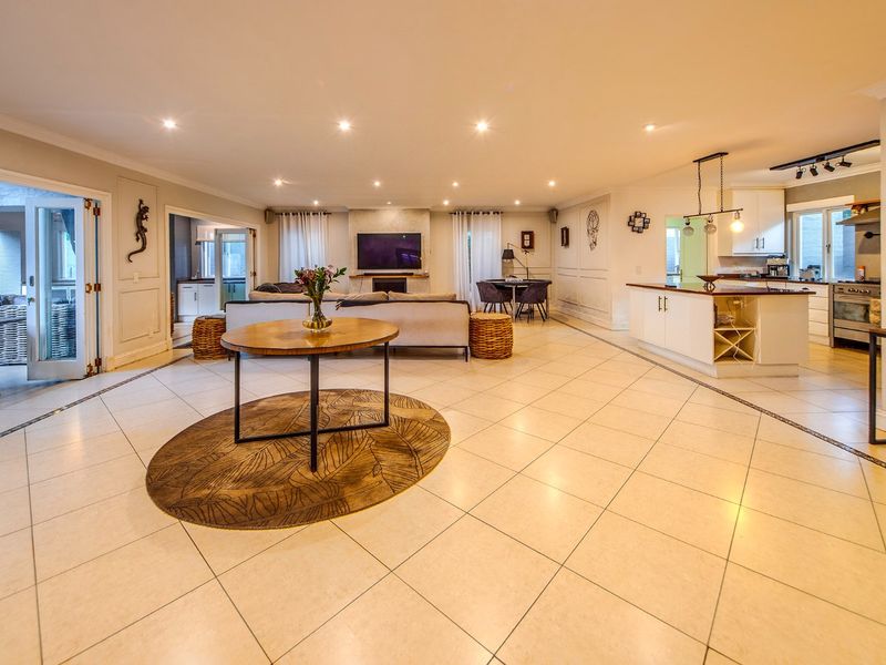 Spacious open-plan living area featuring a modern kitchen with island, tiled floors, recessed lighting, and seamless flow to an outdoor patio through french doors.