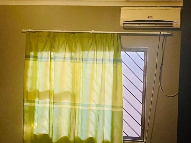 A bedroom featuring an air conditioning unit, security bars on the window, and a ceiling light fixture.