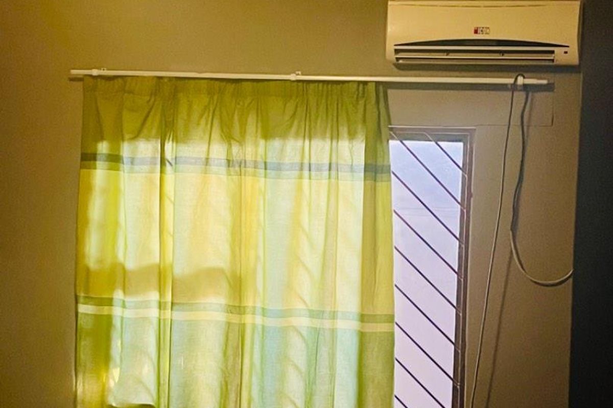 A bedroom featuring an air conditioning unit, security bars on the window, and a ceiling light fixture.