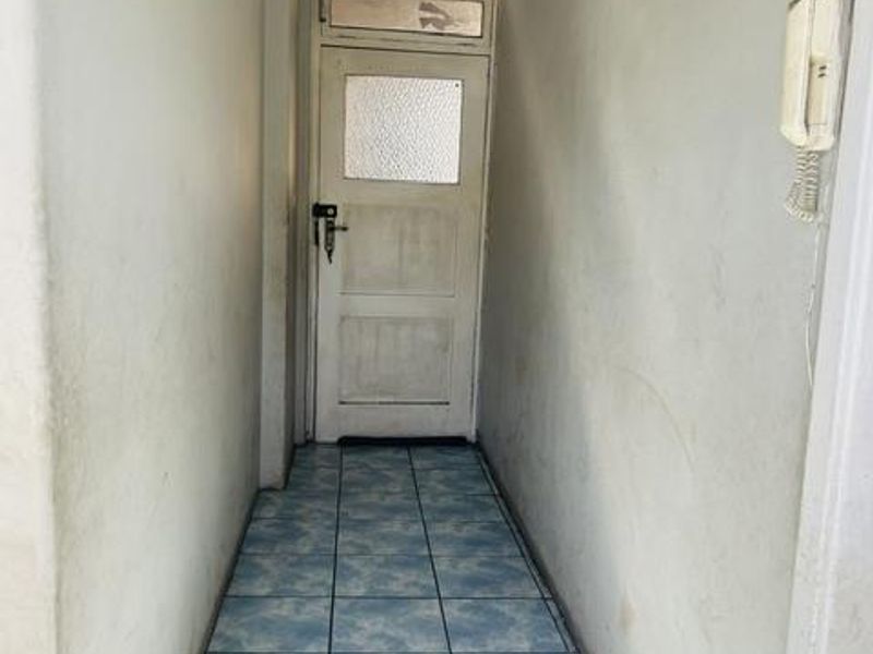 A narrow hallway featuring tiled flooring and an intercom system, leading to a panelled entrance door.