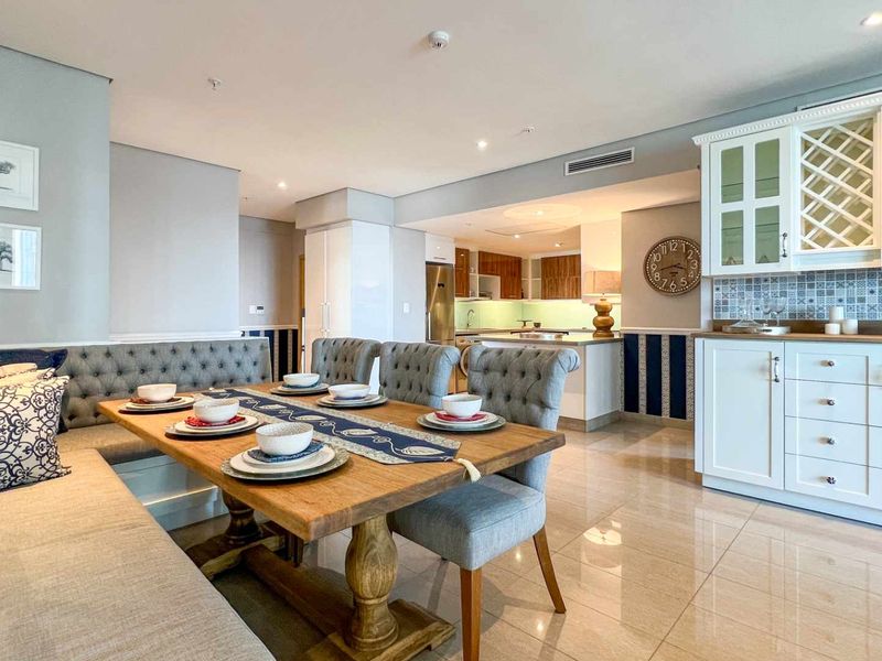Open-plan dining and kitchen area featuring tiled flooring, built-in cabinetry, and recessed lighting in a modern apartment setting.