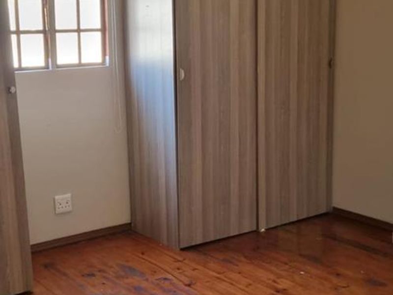 A bedroom featuring polished timber flooring, a built-in wardrobe, and a multi-pane window, offering a blank canvas for interior design.