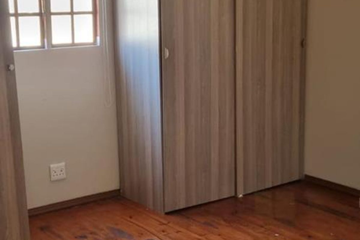 A bedroom featuring polished timber flooring, a built-in wardrobe, and a multi-pane window, offering a blank canvas for interior design.