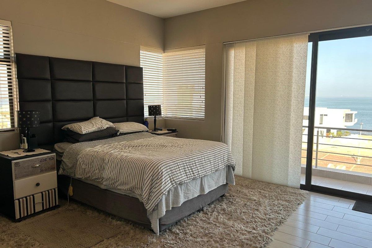 Spacious bedroom featuring tiled flooring, large sliding glass doors leading to a balcony, and venetian blinds, offering natural light and ocean views.