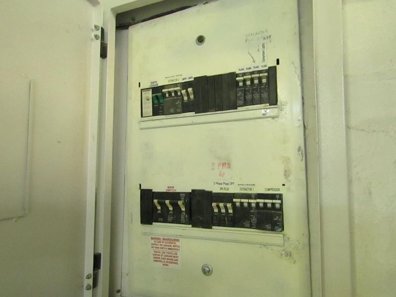 A functional industrial electrical distribution board with clearly labeled circuit breakers for machinery, lighting, and compressor systems.