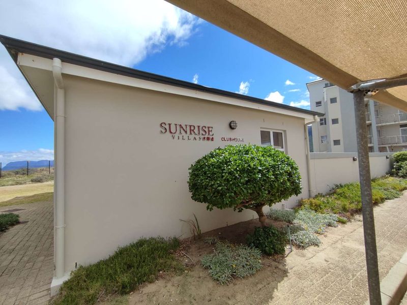 Exterior view of the Sunrise Villas clubhouse building featuring paved walkways and a shade sail structure.