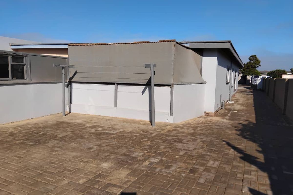 A paved rear exterior area featuring a fixed washing line structure and a covered lean-to section attached to the main building.