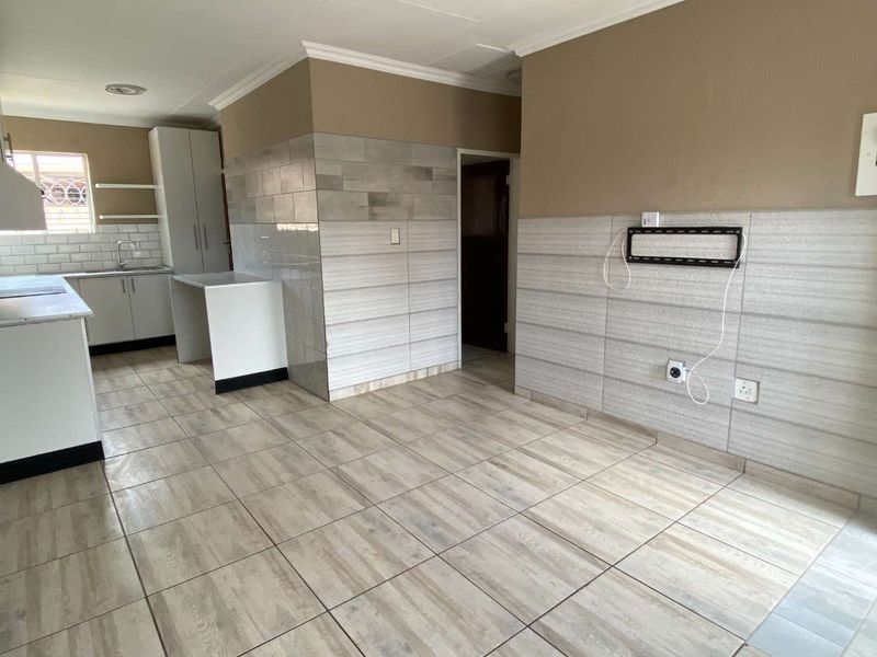 An open-plan living and kitchen area featuring neutral wall tiling, modern floor tiles, and functional kitchen cabinetry in a clean, vacant space.