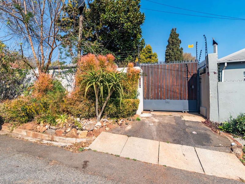 Front exterior view featuring a secure sliding gate, boundary wall with electric fencing, and a paved driveway entrance.