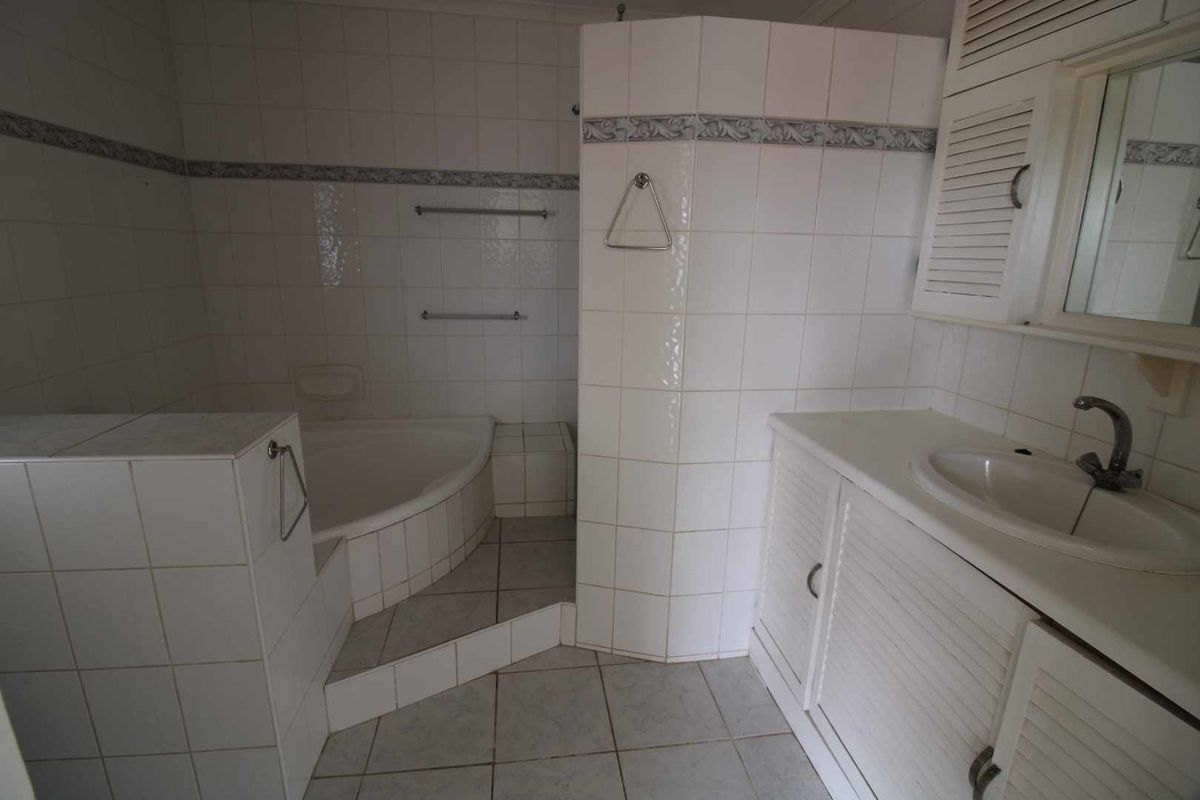 A functional bathroom featuring a built-in corner bathtub, tiled surround, and a vanity unit with a basin and integrated storage.