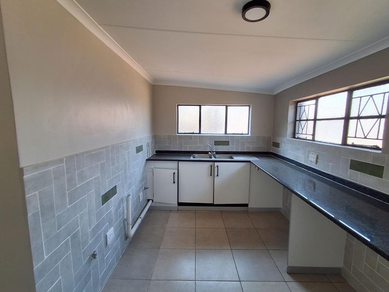 A functional, empty kitchen featuring tiled flooring, a tiled backsplash, laminate countertops, and built-in cabinetry with a stainless steel sink.