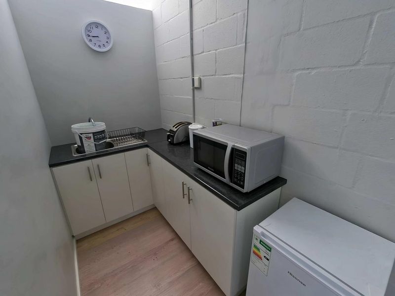 Compact scullery or kitchenette area featuring built-in cabinetry, a stainless steel sink, and laminate countertops within an industrial-style space.