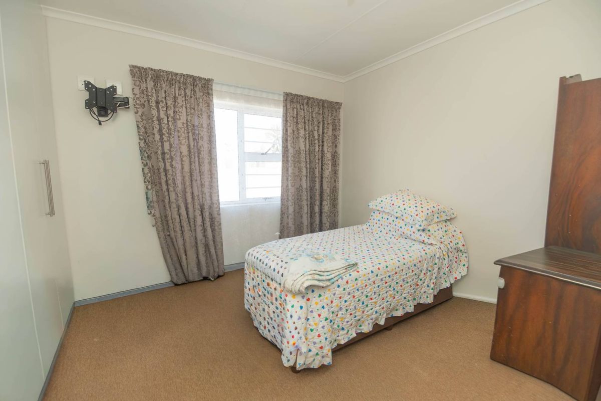 A standard bedroom featuring built-in cupboards, carpeted flooring, and a window with curtain tracks.