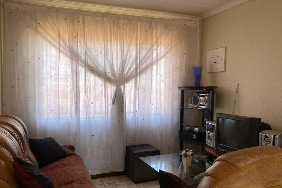 A living room featuring a large window with security bars, tiled flooring, and neutral wall finishes.
