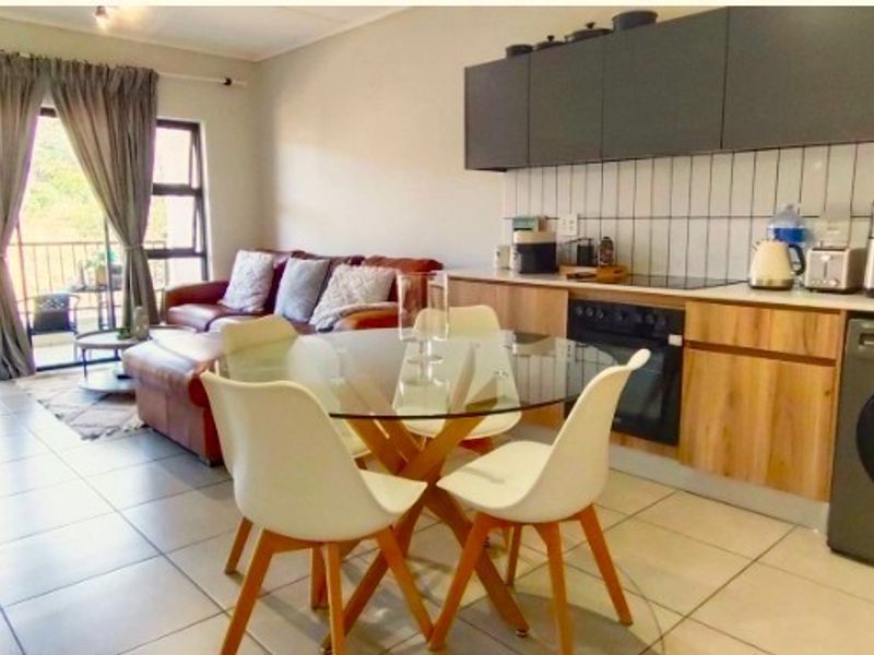 An open-plan living and kitchen area featuring modern cabinetry, tiled flooring, and a sliding door leading to a balcony.