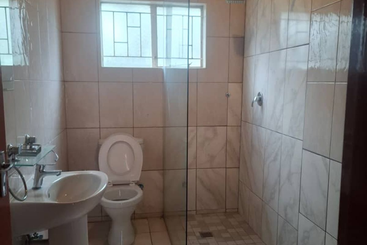 A functional bathroom featuring a walk-in shower with glass screen, pedestal basin, and toilet, finished with neutral wall and floor tiling.