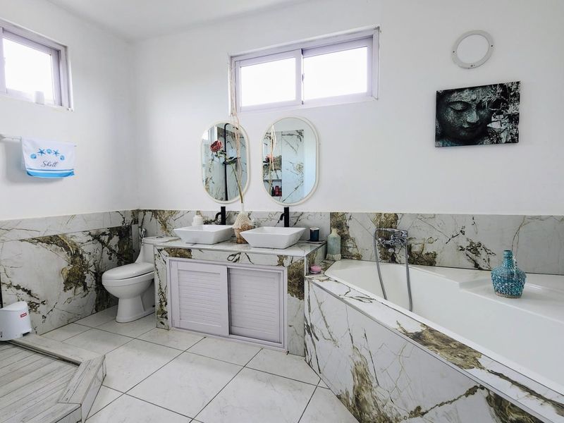 A modern bathroom featuring marble-look wall tiles, a double vanity with vessel sinks, a built-in bathtub, and a separate walk-in shower area.