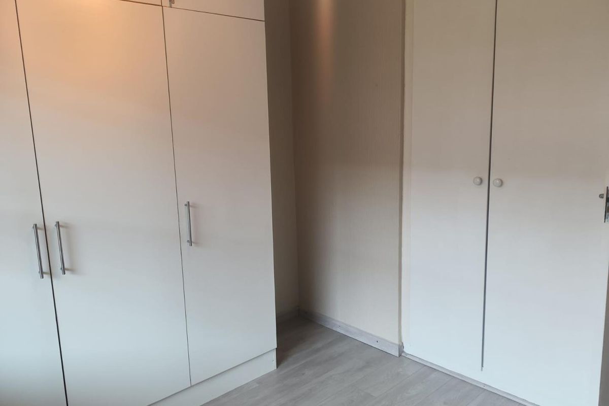 A bedroom interior featuring built-in floor-to-ceiling wardrobes with modern handles and light-toned laminate flooring.