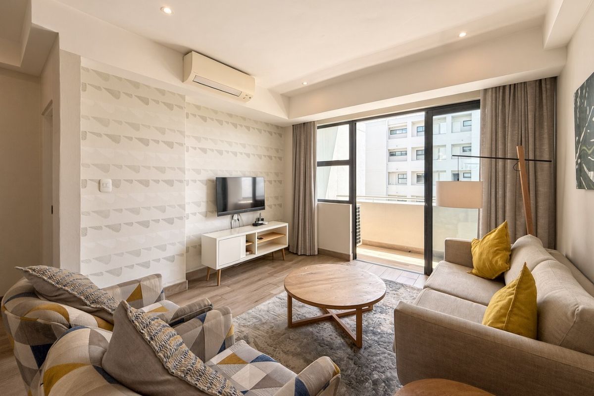 A well-maintained living room featuring tiled flooring, recessed lighting, a wall-mounted air conditioner, and direct access to a private balcony through sliding glass doors.