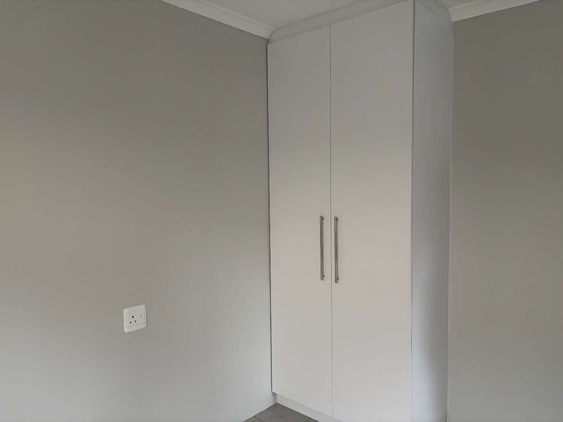 A clean, neutral bedroom featuring a modern white built-in wardrobe and a standard electrical outlet.