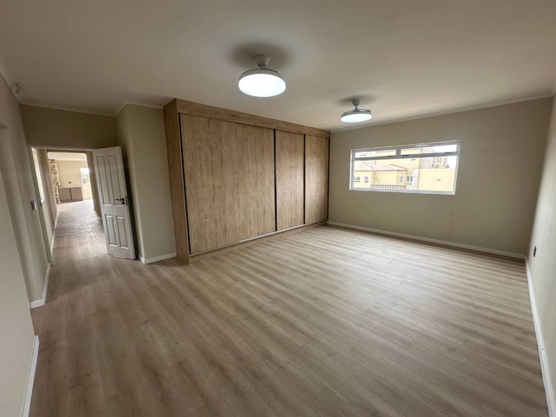 A spacious, empty bedroom featuring modern light-toned laminate flooring, a large built-in wardrobe with wood-grain finish, and neutral wall paint.