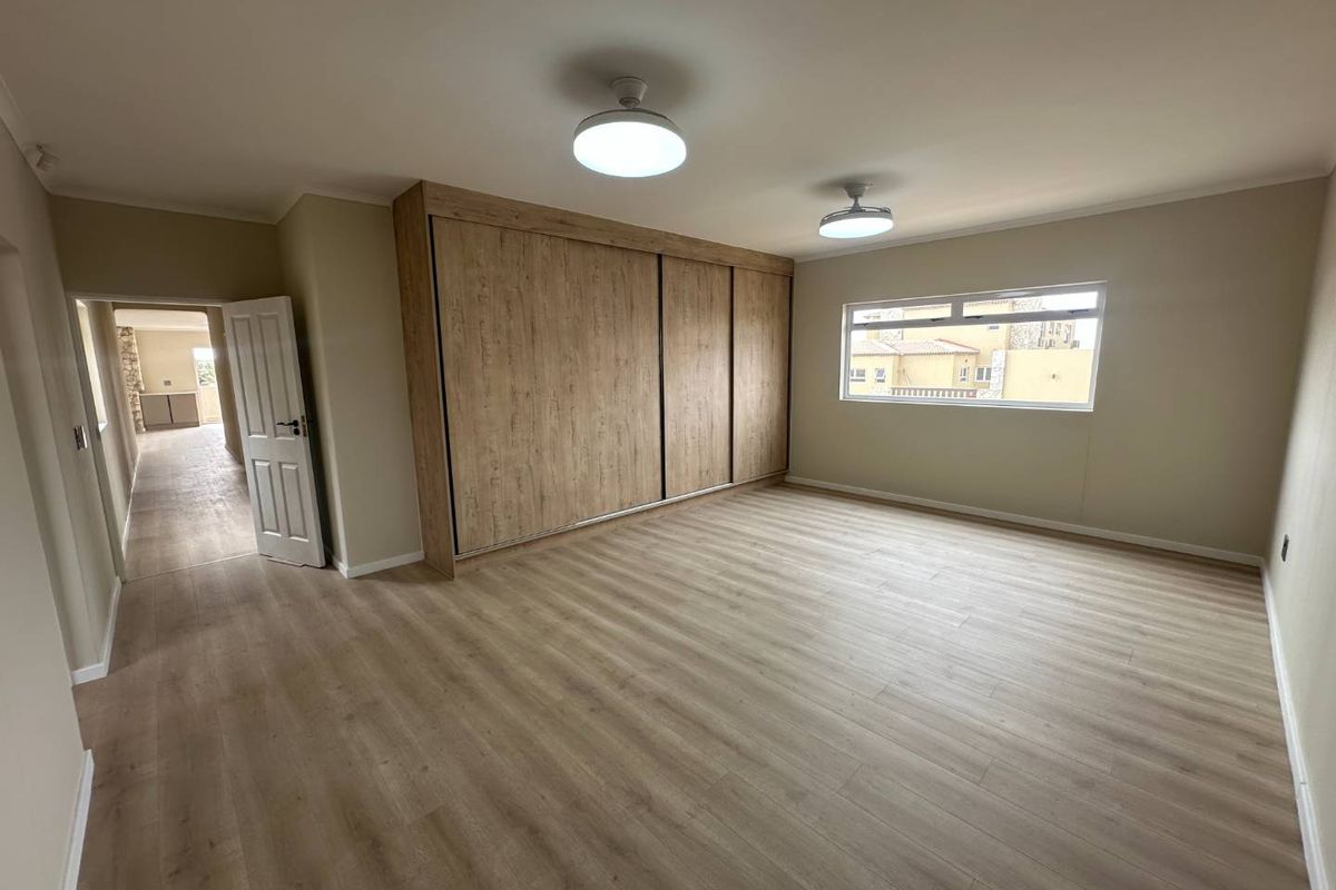 A spacious, empty bedroom featuring modern light-toned laminate flooring, a large built-in wardrobe with wood-grain finish, and neutral wall paint.