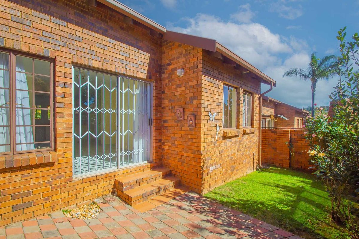 Rear view of the townhouse featuring a paved patio area, brick facade, and sliding glass doors with security gates leading to a private garden.