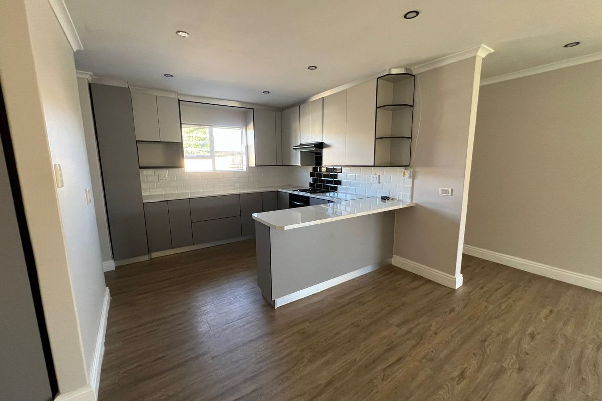 Modern kitchen featuring grey cabinetry, white quartz countertops, subway tile backsplash, integrated appliances, and recessed lighting, set within an open-plan living space.