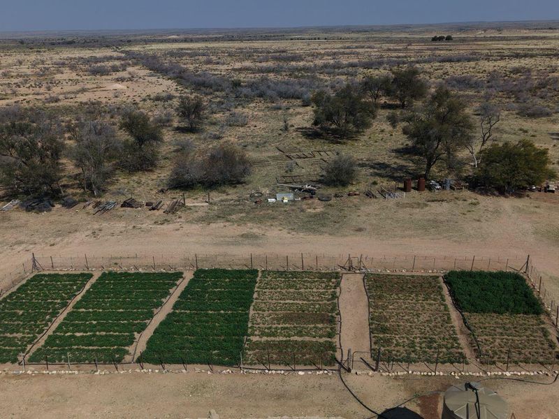 Aerial view of a fenced agricultural vegetable garden plot on a farm, featuring irrigation infrastructure and a water storage tank.